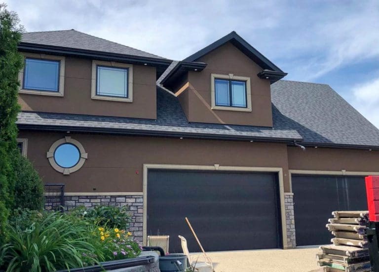 Edmonton Stucco A large brown two-storey house with multiple windows, a dark gray roof, and an attached garage. The exterior combines stucco, stonework, and stone materials. Some construction materials are Contractors
