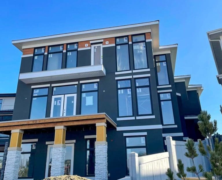 Edmonton Stucco Modern two-story house featuring acrylic stonework, with a mix of dark gray and white paneling, extensive windows, and under a clear blue sky. Contractors