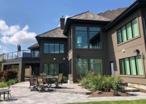 Edmonton Stucco A modern two-story house with large windows and stucco exterior walls. It features a landscaped garden and a patio area with outdoor furniture under clear blue skies. Contractors