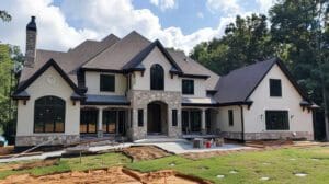 Edmonton Stucco A large, newly constructed house with multiple gabled roofs and a mix of stone and Edmonton Stucco Experts exteriors, set against a backdrop of trees under a clear sky. Landscaping is Contractors